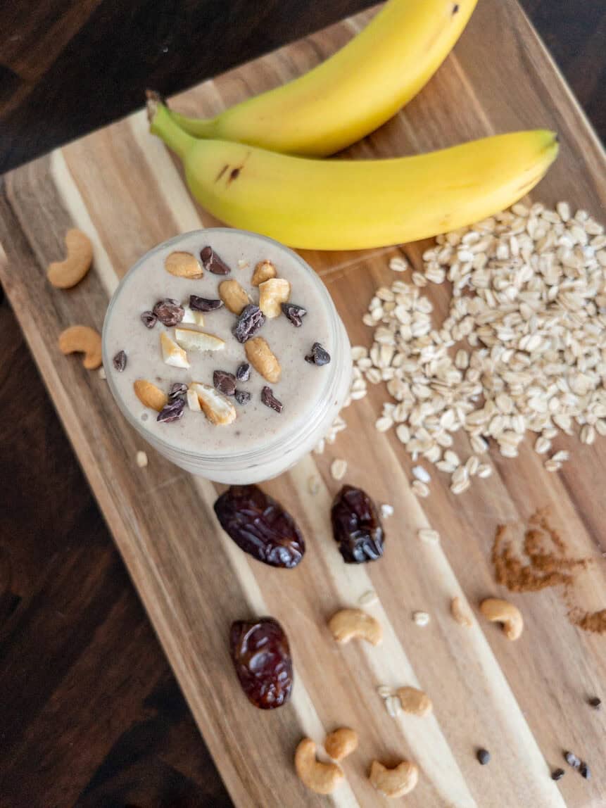 Cashew date smoothie surrounded by its ingredients like bananas, dates, cashews, oats, and cinnamon.