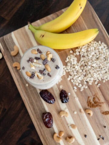 Cashew date smoothie surrounded by ingredients like bananas, dates, cashews, oats, and cinnamon.