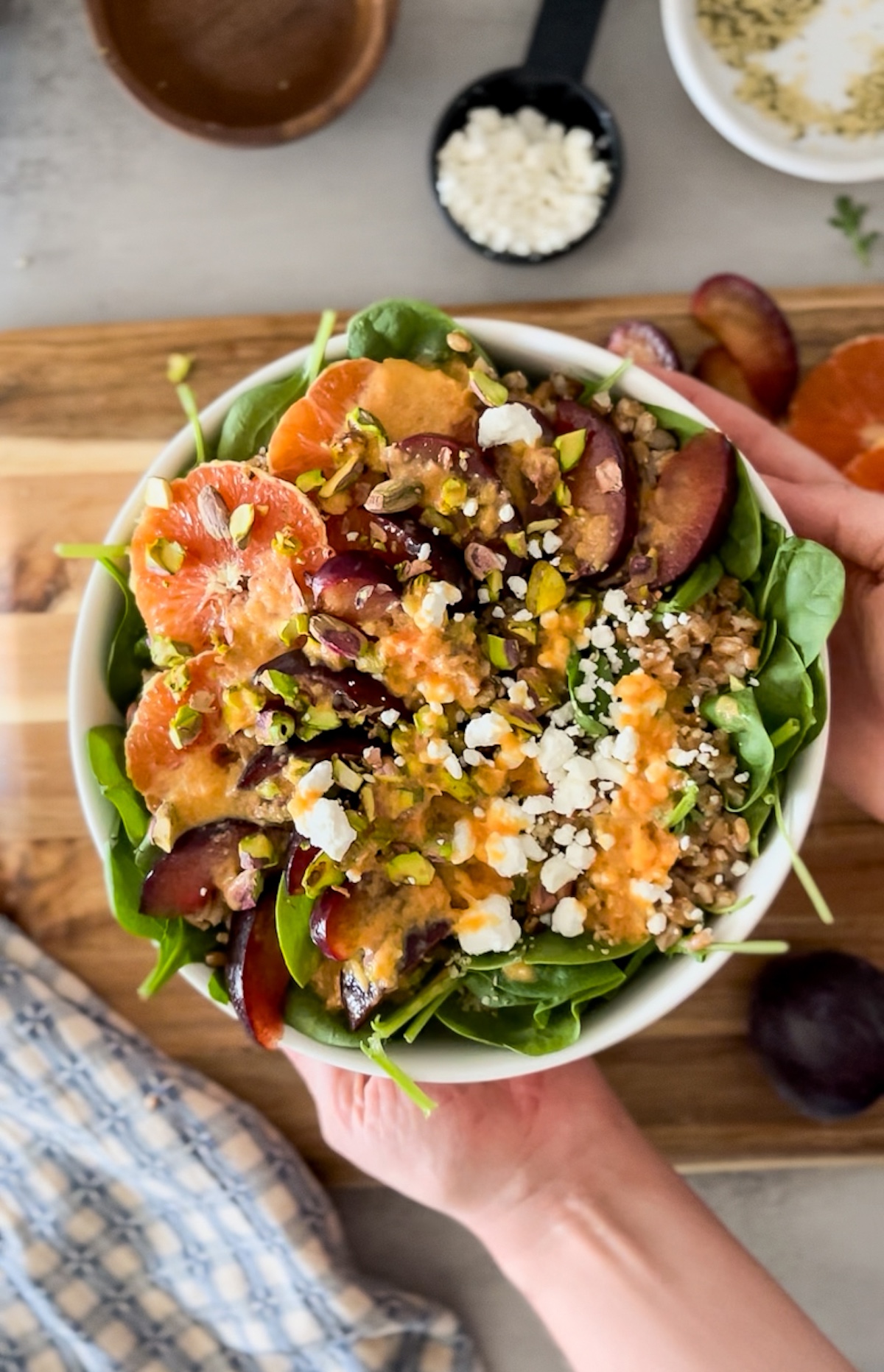 top down shot of hands holding plum citrus arugula salad with citrus dressing