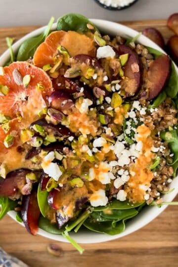 top down shot of plum citrus arugula spinach salad with citrus dressing drizzle on a wooden board
