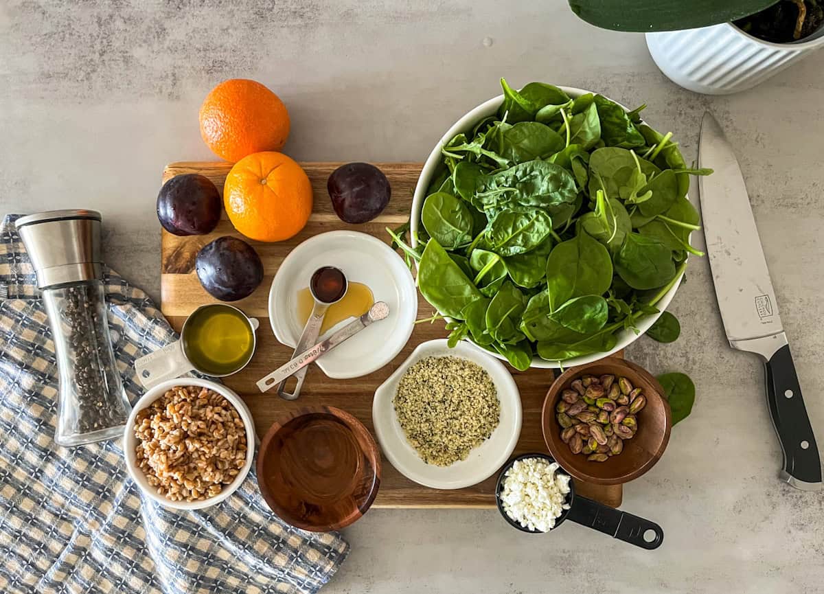 top down shot of plum citrus arugula spinach salad ingredients including oranges, plums, spinach, farro, pistachios, etc.