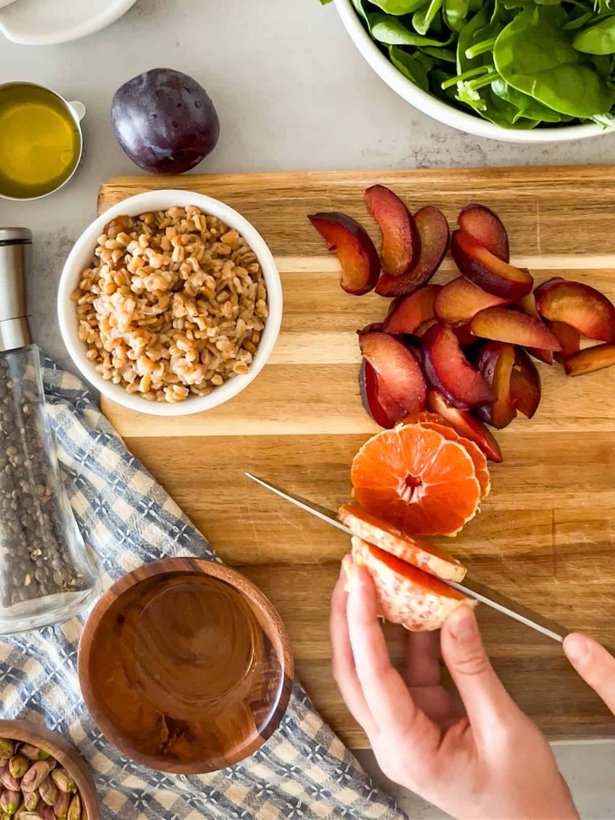 slicing oranges and plums on wooden board, also features a small bowl of farro