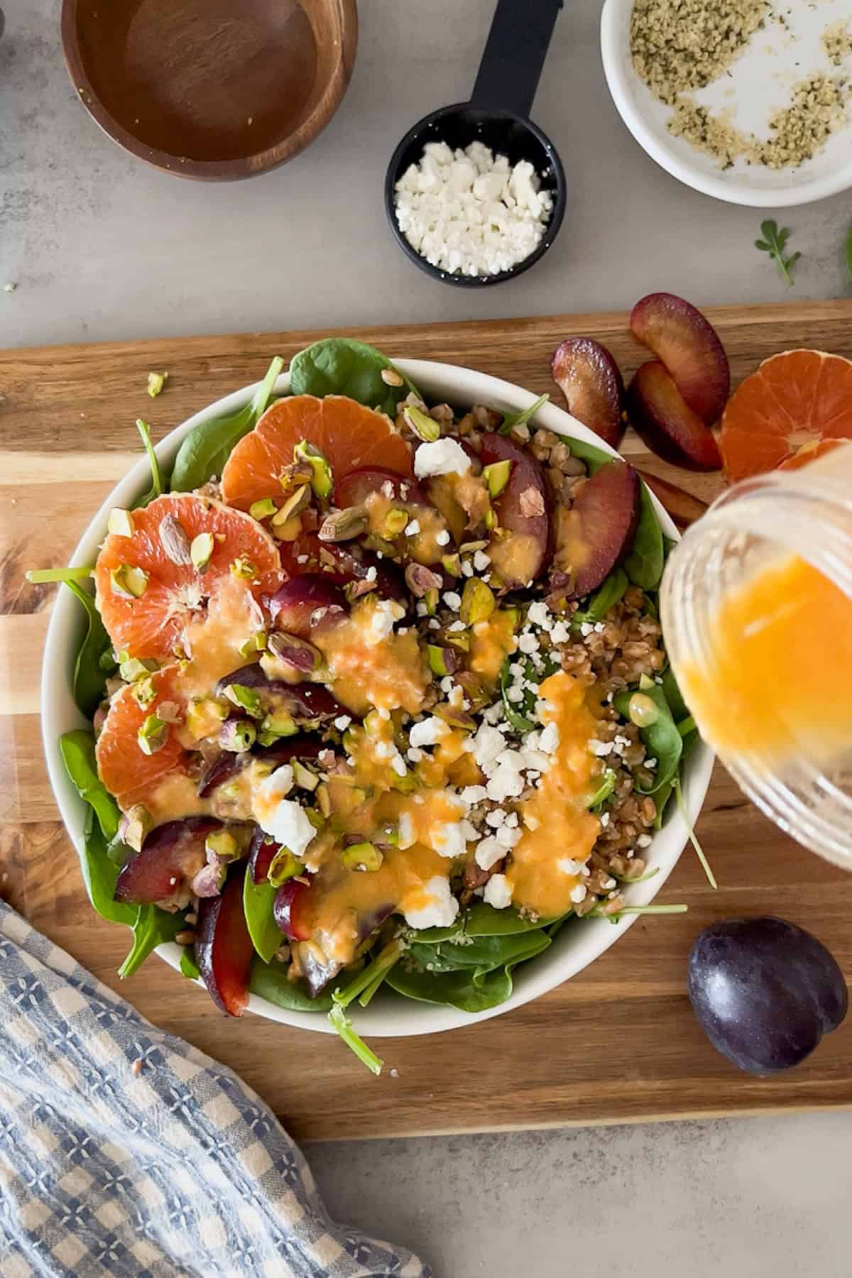 citrus dressing being drizzled on fully assembled plum citrus arugula spinach salad